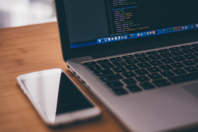 Laptop displaying code with smartphone adjacent.